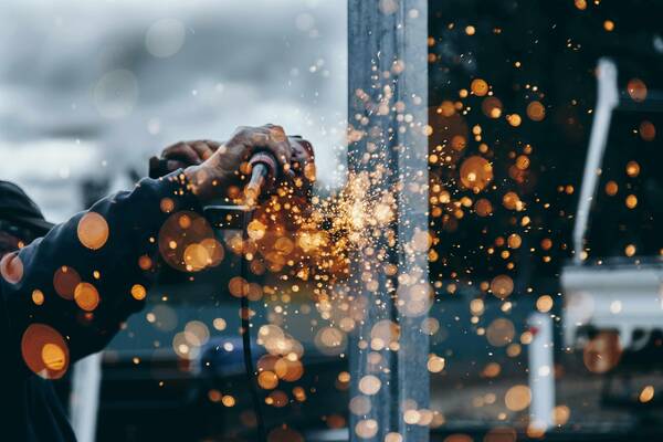 Close-up of hands using a power tool, sending a shower of bright orange sparks into the air.